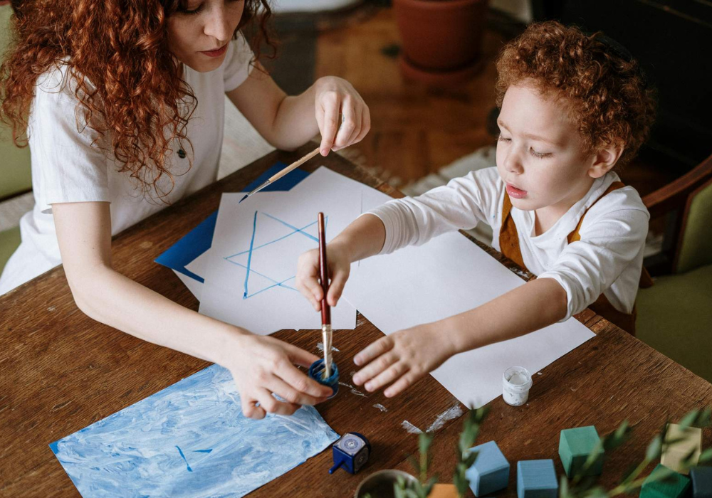 Two people painting with watercolors at a table, focusing on a blue geometric design